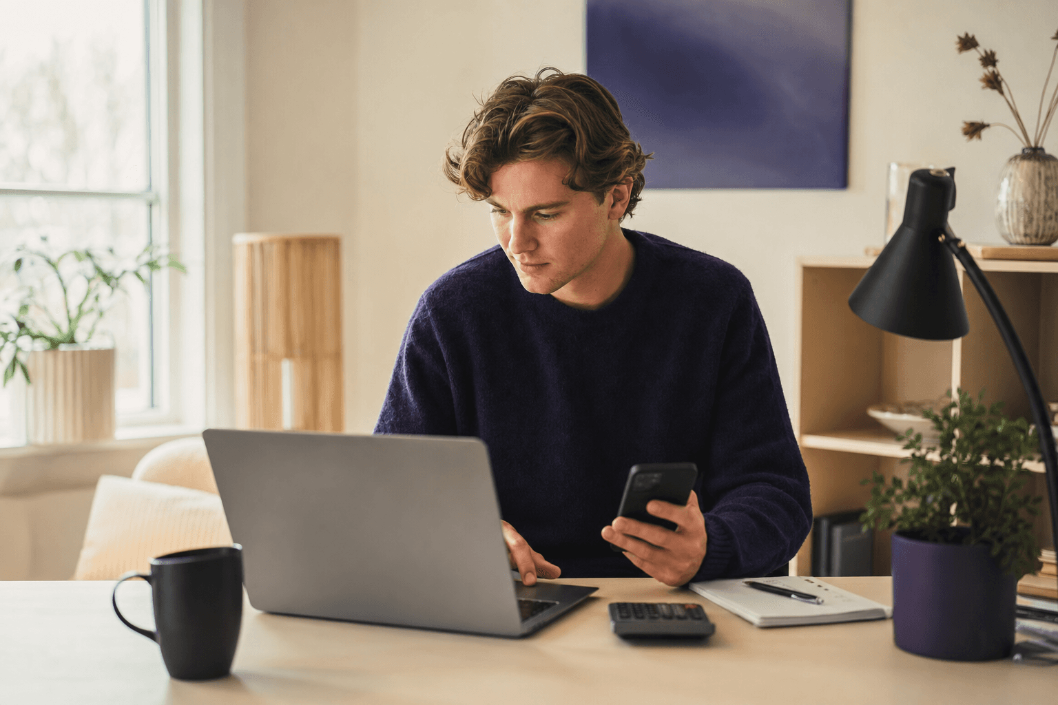 Ung norsk influencer sitter ved et hjemmekontor og går gjennom egen økonomi på en laptop, med mobil, notatbok og kalkulator ved siden av
